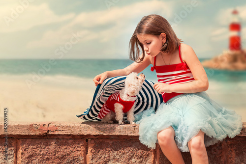 A girl with a poodle dog sits on the background of a lighthouse by the sea photo