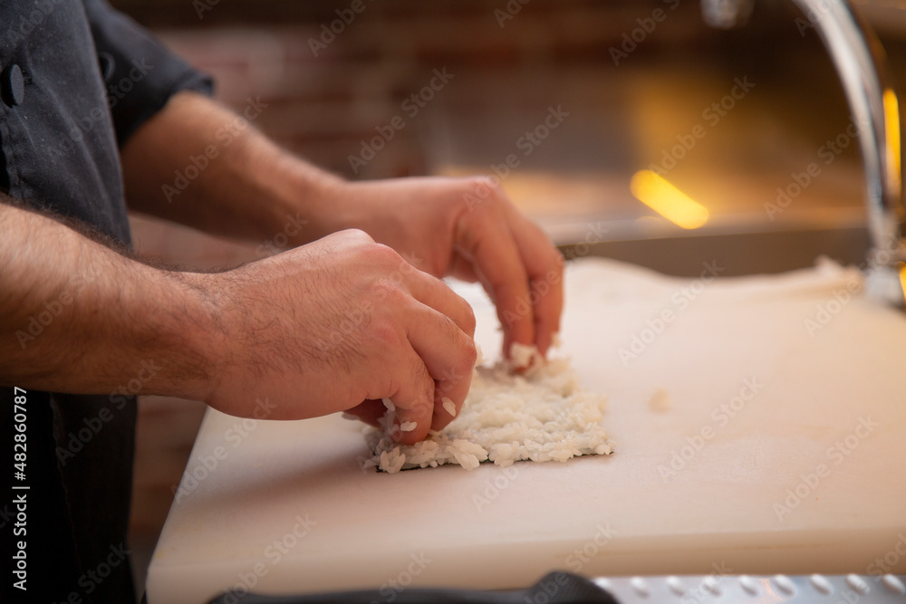 Anonymous spreading rice on nori sheet making roll sushi