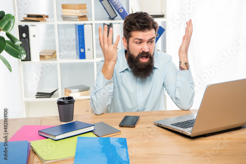 Angry businessman working on laptop at office desk, work