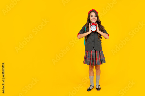 happy childhood. child with alarm clock. copy space. cheerful teen girl carry backpack.