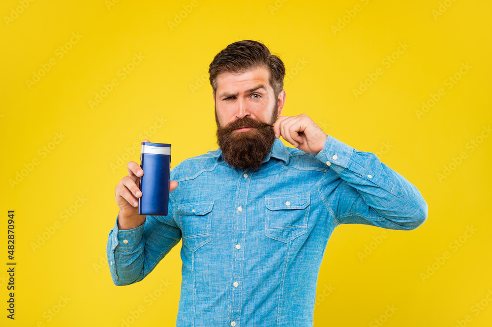 brutal bearded man hold hair conditioner bottle, presenting toiletries. touch moustache. brutal bearded man hold hair conditioner bottle, presenting toiletries. touch moustache.
