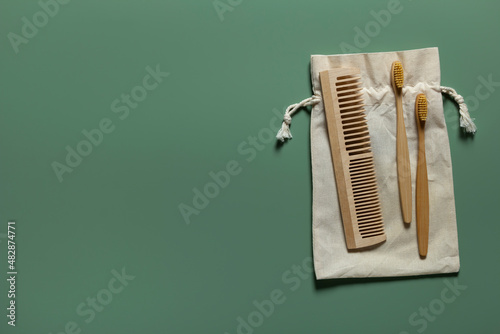 Natural bathroom accessories wooden toothbrushes, hair comb, reusable cotton bag on green background with copy space.