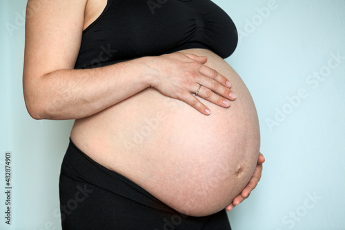 Pregnant woman with large belly, female holding hands her body
