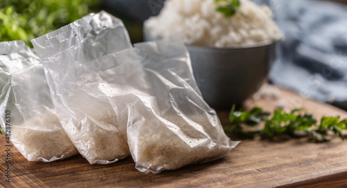 Raw rice in plastic bags on wooden background and cooked rice in bowl