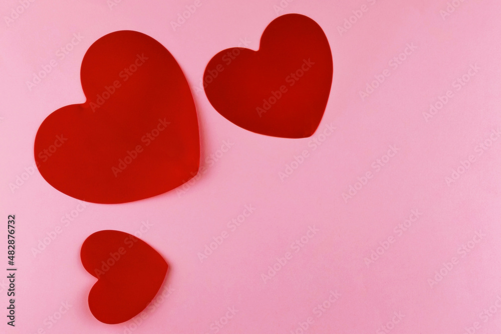 Three red hearts on pink pastel paper textured background. Top view. Flat lay. Close up. Text copy space.