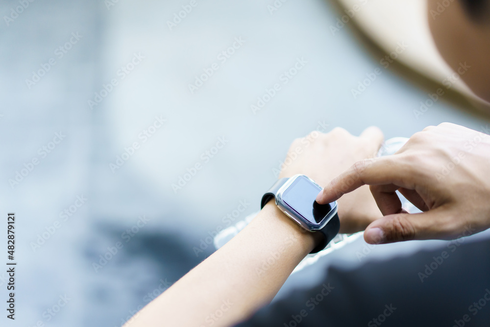 Active Asian young sportsman using a smartwatch or smart fitness band to track his outdoor workout and activities. Active Asian young sportsman using a smartwatch or smart fitness band to track his outdoor workout and activities.