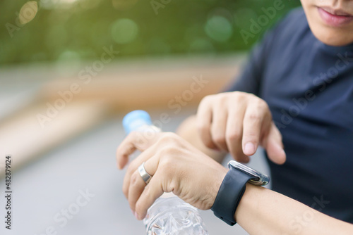 Active Asian young sportsman using a smartwatch or smart fitness band to track his outdoor workout and activities.