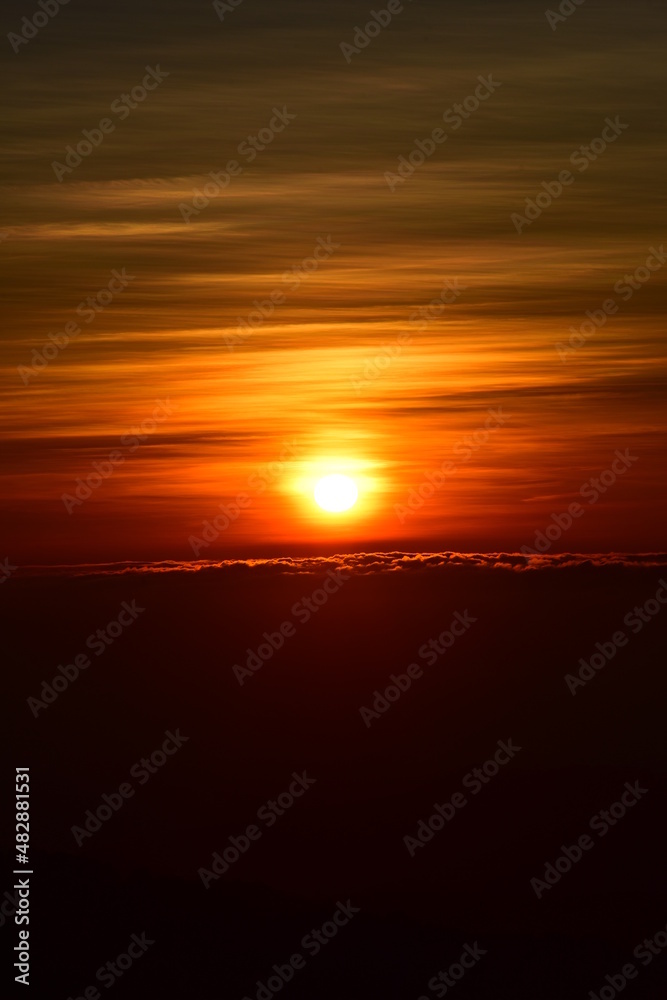 Fototapeta premium The sun set behind thick forests followed by mountains.