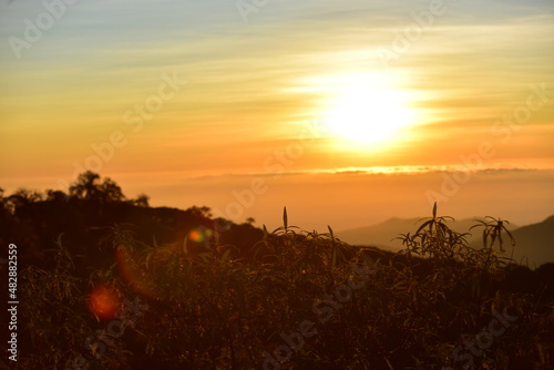 The sun set behind thick forests followed by mountains.