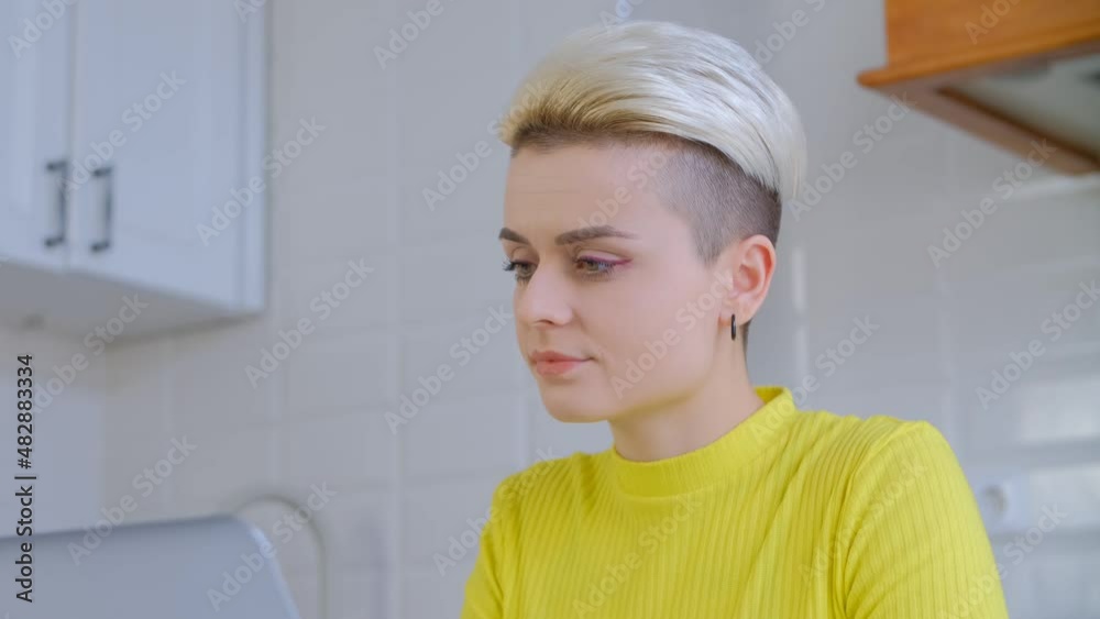Young woman working on laptop. Video portrait of tom boy female with dyed shor hair doing distant work on notebook pc on lockdown. Freelancer person using computer for online education Young woman working on laptop. Video portrait of tom boy female with dyed shor hair doing distant work on notebook pc on lockdown. Freelancer person using computer for online education