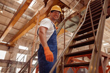 Cheerful male builder standing on stairs in workshop