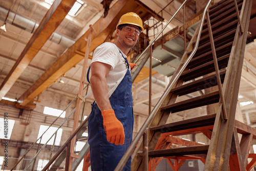 Cheerful male builder standing on stairs in workshop