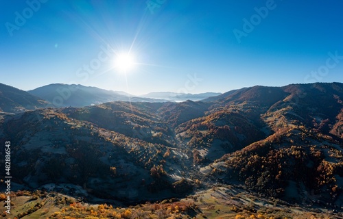 Sun rises above high mountain peaks with yellowed trees