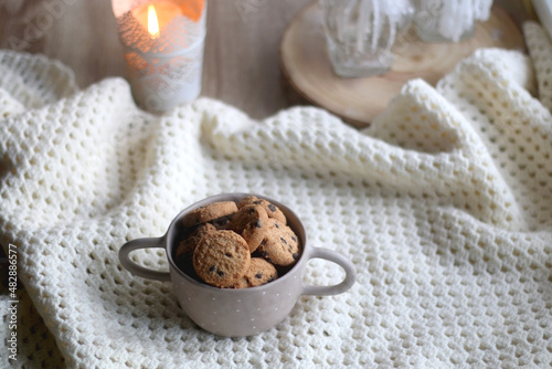 Bowl of chocolate chip cookies, soft blanket and candle holders with lit candles. Hygge at home. Selective focus.