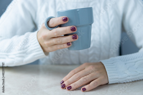 Unrecognizable girl leaning on a table with a gray mug in one hand