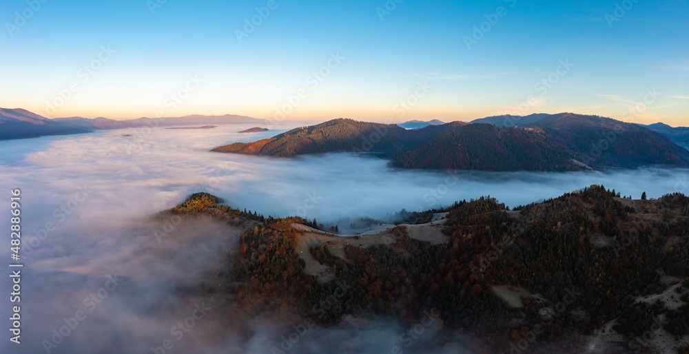 Thick fog among peaks of high autumn mountains at sunrise
