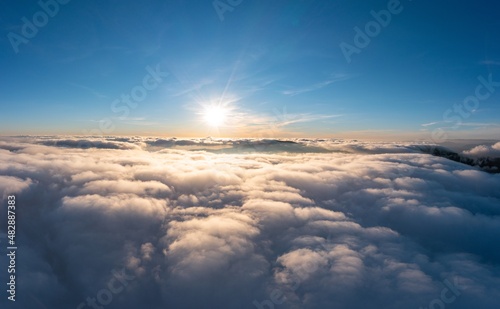 Fototapeta Naklejka Na Ścianę i Meble -  Sun shining brightly above white fluffy clouds at sunrise