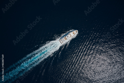 Luxury white mega yacht fast movement on dark water in the ocean top view. Big yacht in the sea drone view. Big white super boat moves on the water leaving a white trail aerial view. © Berg