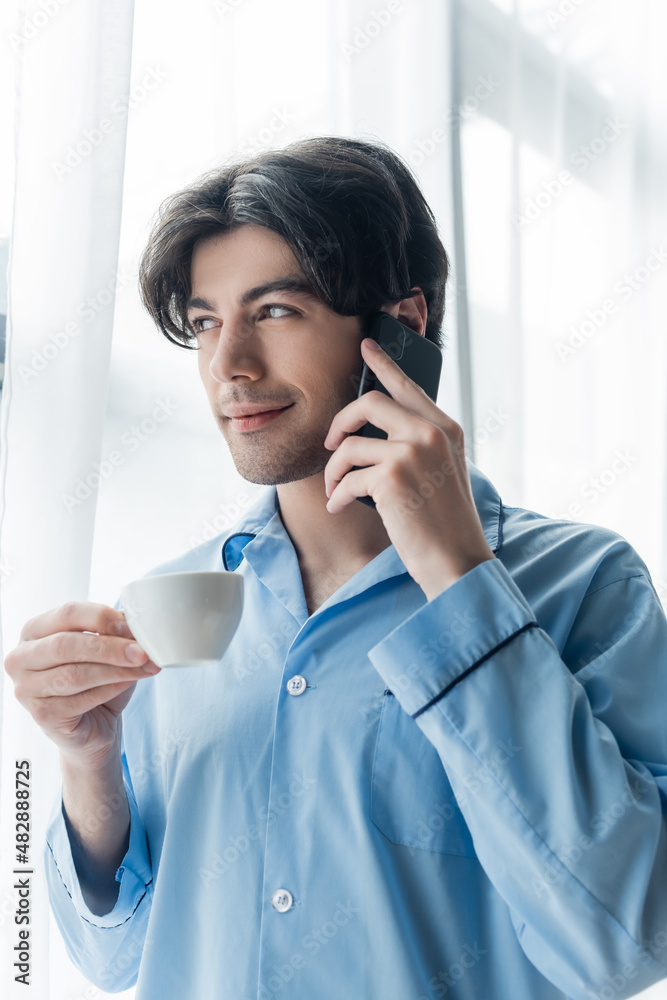 smiling man in blue pajamas holding coffee cup while talking on mobile phone. smiling man in blue pajamas holding coffee cup while talking on mobile phone.