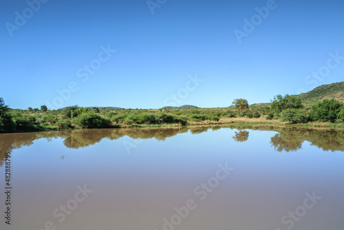 Landscape view of a lake surrounded by mountains and green savanna grassland, Pilanesburg Nature Reserve, North West Province, South Africa