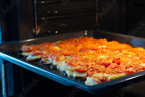 Juicy meat with potatoes, tomatoes and cheese is in the oven, closeup