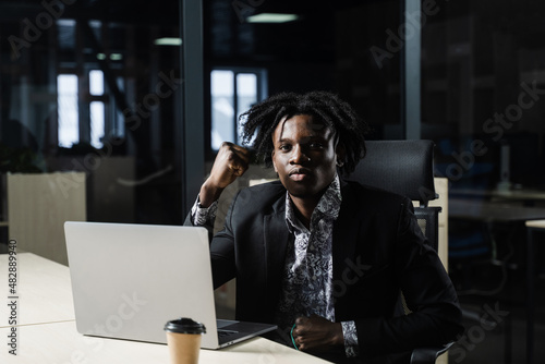 Happy black man clenched fists and rejoice finishing his online job on laptop. Working online in coworking space.