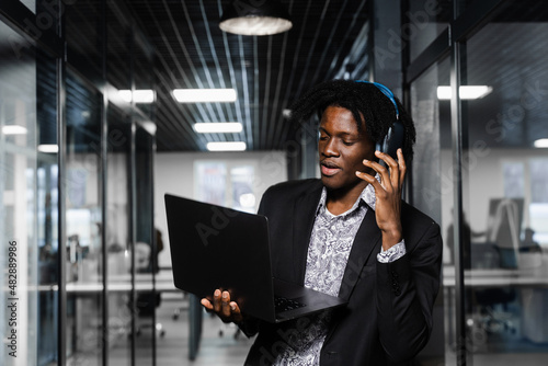 Cheerful black man in headphones listen audio podcast and enjoy music. Handsome african man with laptop in the office. Party concept.