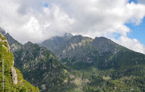 Sharp rocky high ridges of mountain ranges covered with trees and vegetation under a cloudy sky. High Tatras  Slovakia