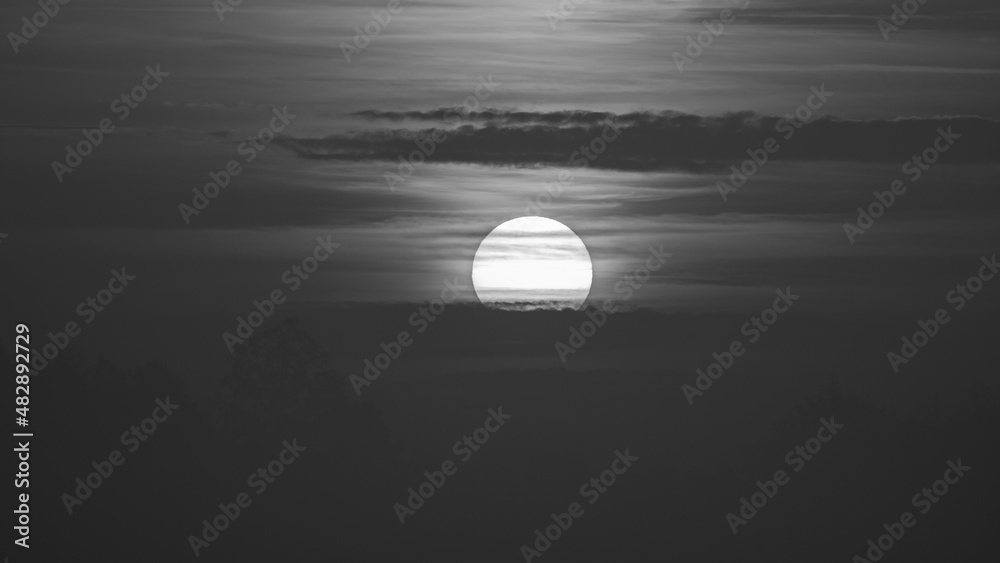 Beautiful wild sunrise and cloudy sky. The sun behind the clouds. Black and white picture Beautiful wild sunrise and cloudy sky. The sun behind the clouds. Black and white picture
