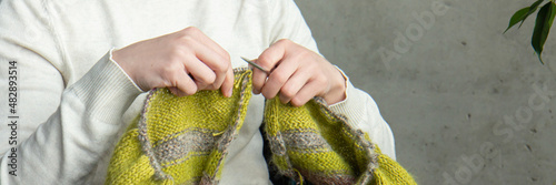 Young woman knitting warm colorful sweater at home. Concept of needlework. Close up. Banner