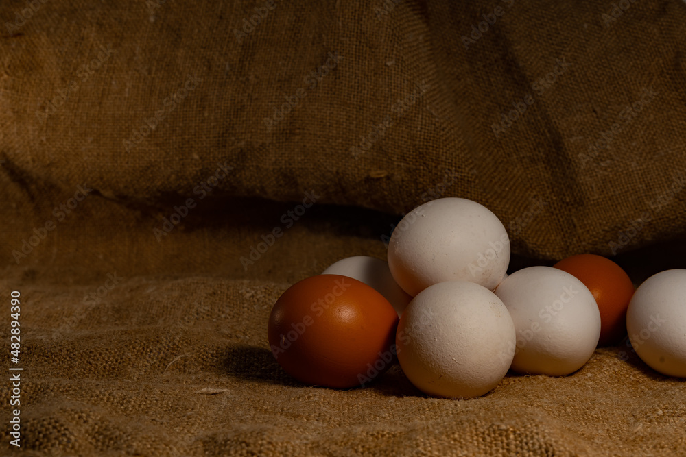 A mountain of white and brown eggs, on a textured burlap backing. The background and the backing of burlap, on which lies a pile of fresh chicken eggs. A mountain of white and brown eggs, on a textured burlap backing. The background and the backing of burlap, on which lies a pile of fresh chicken eggs.