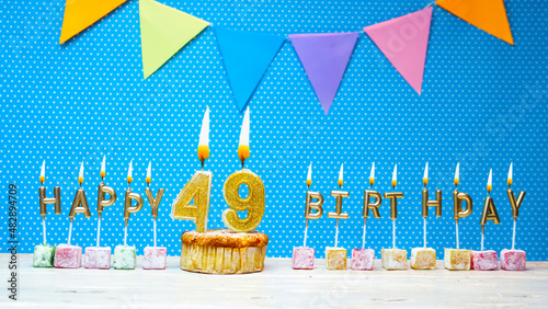 Congratulations on your birthday from the letters of candles number 49 on a blue background with polka dots white copy space. Happy birthday muffin with burning golden color candle for forty nine. photo