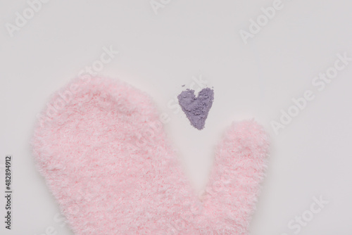 Minimal flat lay composition of massage mitten washcloth and a heart made of violet powder on a white background. Concept of zero waste