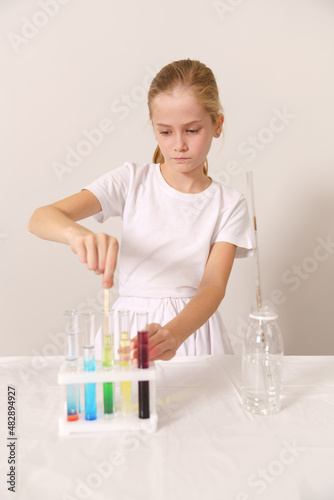 a white girl in a white T-shirt mixes colored dyes in test tubes