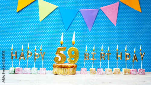 Congratulations on your birthday from the letters of candles number 59 on a blue background with polka dots white copy space. Happy birthday muffin with burning golden candle for fifty nine years photo