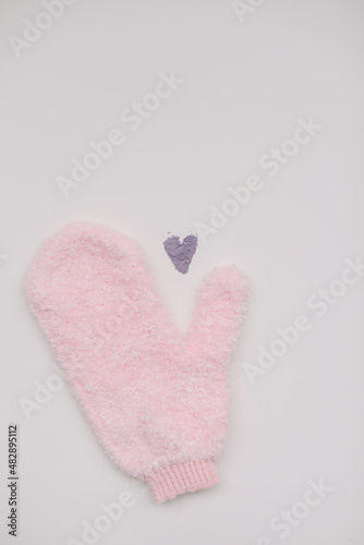 Minimal flat lay composition of massage mitten washcloth and a heart made of violet powder on a white background. Concept of zero waste