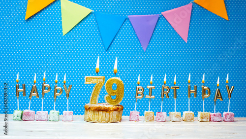 Happy birthday from number 79 candle letters on a blue background with white polka dot copy space. Happy birthday cupcake with burning golden candle for seventy nine years old. photo