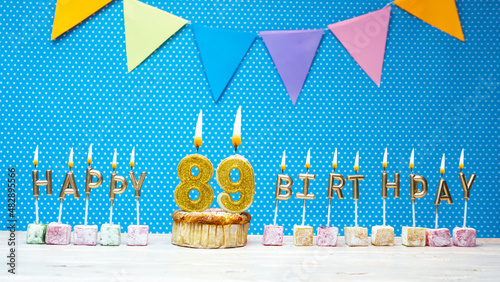Happy birthday from candle letter number 89 on blue background with white polka dot copy space. Happy birthday cupcake with golden candle for eighty nine years. photo