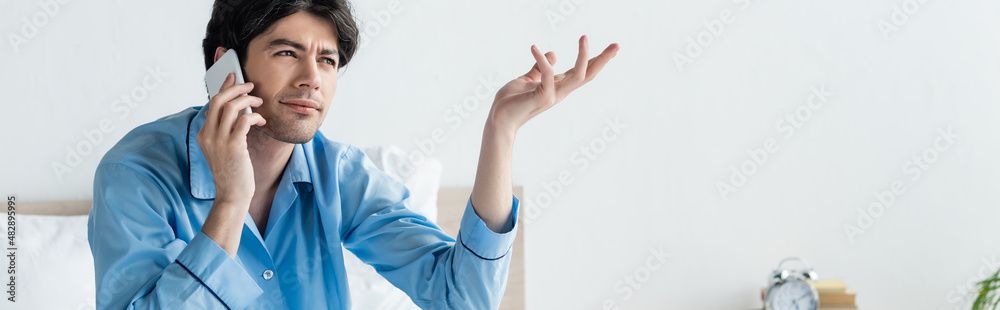 thoughtful man gesturing while talking on mobile phone in bedroom, banner. thoughtful man gesturing while talking on mobile phone in bedroom, banner.