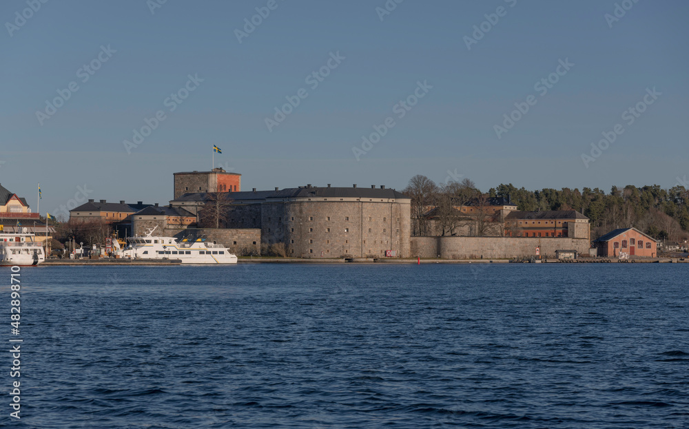 Panorama view of the defence fortress Vaxholms kastell and the ness pier of the district town of Vaxholm with commuting boats a sunny winter day in the archipelago of Stockholm