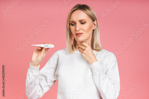 Young woman having flu taking thermometer. Isolated over pink background. Beautiful young woman is sick with a high temperature  a thermometer  isolated close-up. Cold  flu concept.