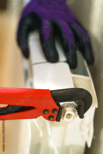 a man with a gas key repairs a white radiator of the heating system. A man in purple gloves