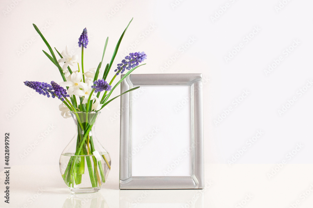 Beautiful flowers bouquet in glass vase and empty photo frame on the table. Muscari and white hyacinth. Mock-up for design. Beautiful flowers bouquet in glass vase and empty photo frame on the table. Muscari and white hyacinth. Mock-up for design.