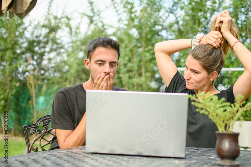 Emotion. Young caucasian couple scared looking at their laptop.