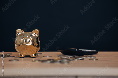 Golden piggy bank with calculator and coins on wooden table