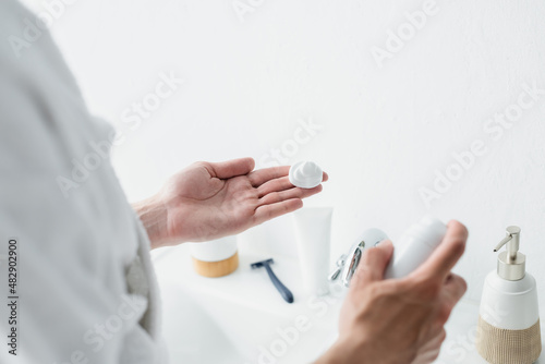 cropped view of man holding shaving foam near blurred toiletries and safety razor.