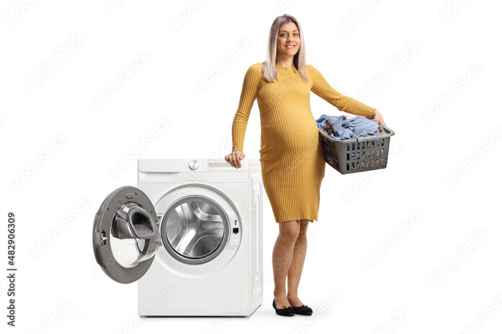 Pregnant woman with a laundry basket leaning on a washing machine