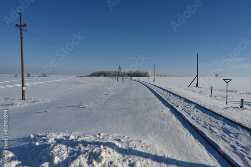 The railway goes into the distance towards the forest on a frosty sunny day.