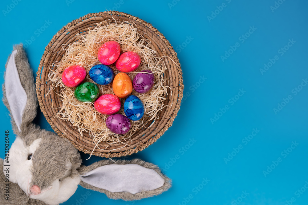 Easter bunny with colored eggs in a basket on a blue background. Easter concept. Copy space