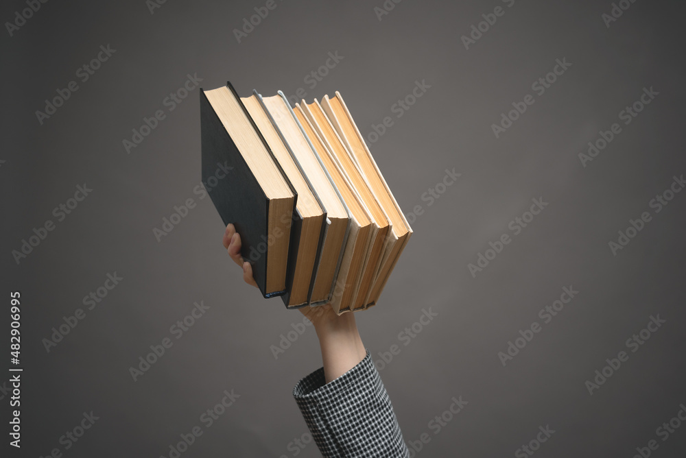 Stack of books in female hand close up on the gray background. Stack of books in female hand close up on the gray background.